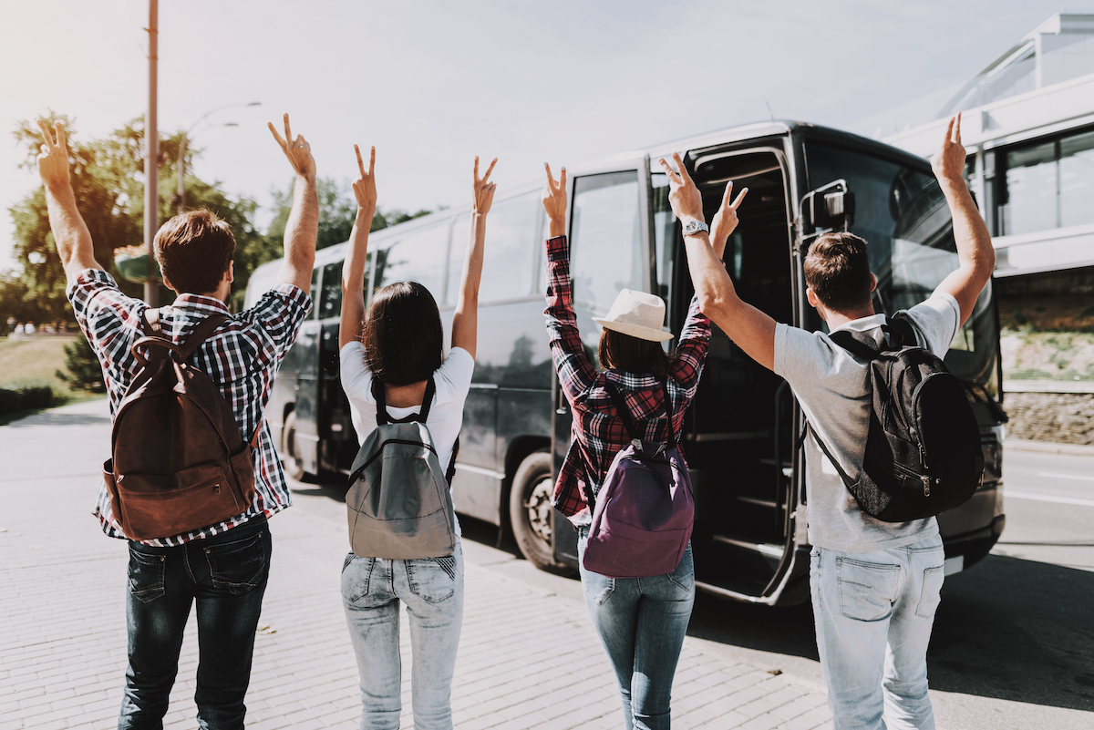 Young People having Fun in front of Tour Bus. Excited Young People. Group of Friends with Backpacks having Fun Together. Traveling, Tourism and People Concept. Happy Travelers on Summer Vacation